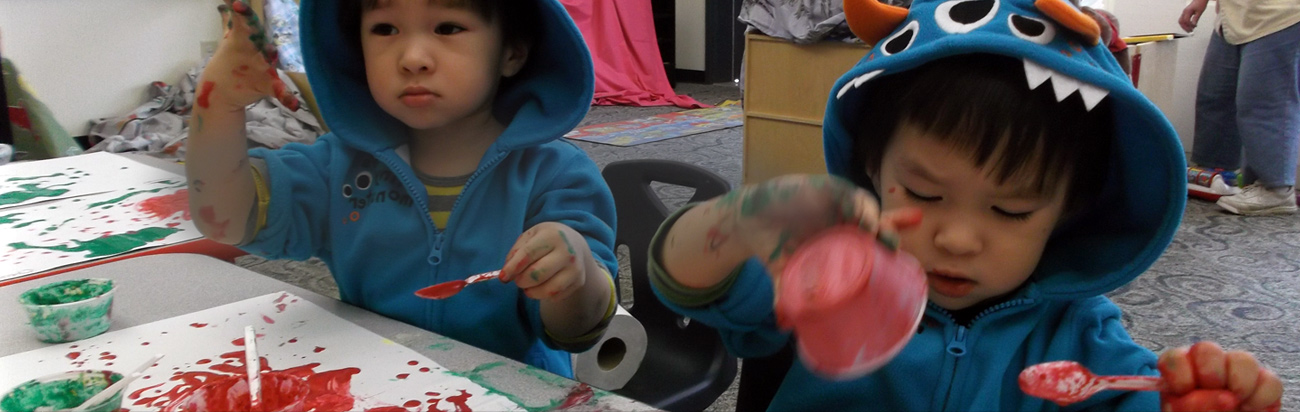 Two young children wearing blue hoodies covered in red and green paint.